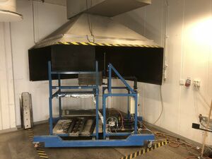 A photo that shows the LIFT apparatus placed beneath one of the hoods in the fire lab.
